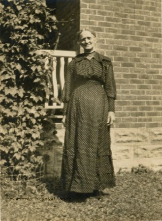 Archival full-length outdoor portrait of Charlotte Emily Lundy standing beside a brick wall