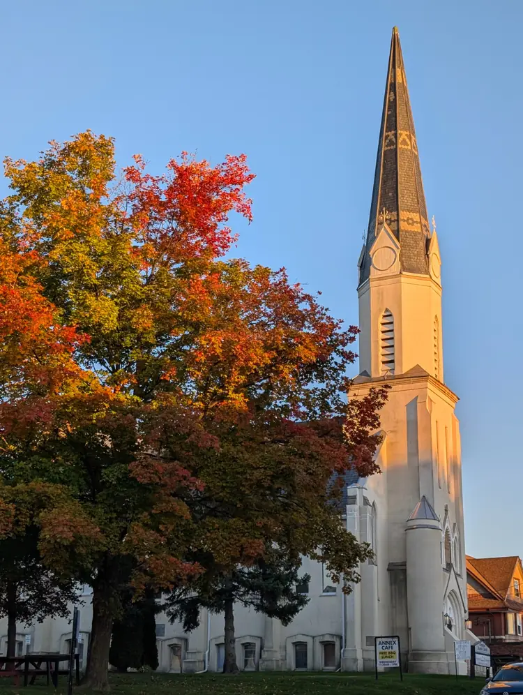 The spire of Newmarket's historic Christian Baptist Church glowing in evening light beside autumn trees